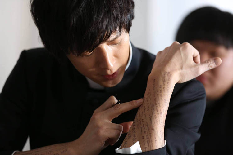 Kang Dong Won plays Deacon Choi in the Korean film The Priests. Here we can see him cheating on an exam. Tsk! I wonder how long it took the makeup person to write all that text on his arm? I bet there are many fan girls who would have done that job for free. (CJ Entertainment photo)