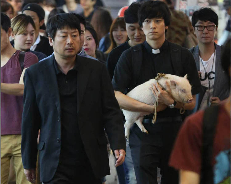 Kim Yun Seok, left, and Kang Dong Won in a scene from the Korean film The Priests. I wonder if those people are all extras, or if they are just regular folks walking down the street? Some of them do seem to be laughing - maybe because of the pig? (CJ Entertainment photo)